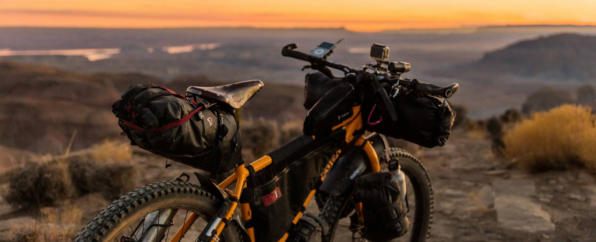 A loaded bikepacking bicycle, set against a scenic desert landscape at sunset